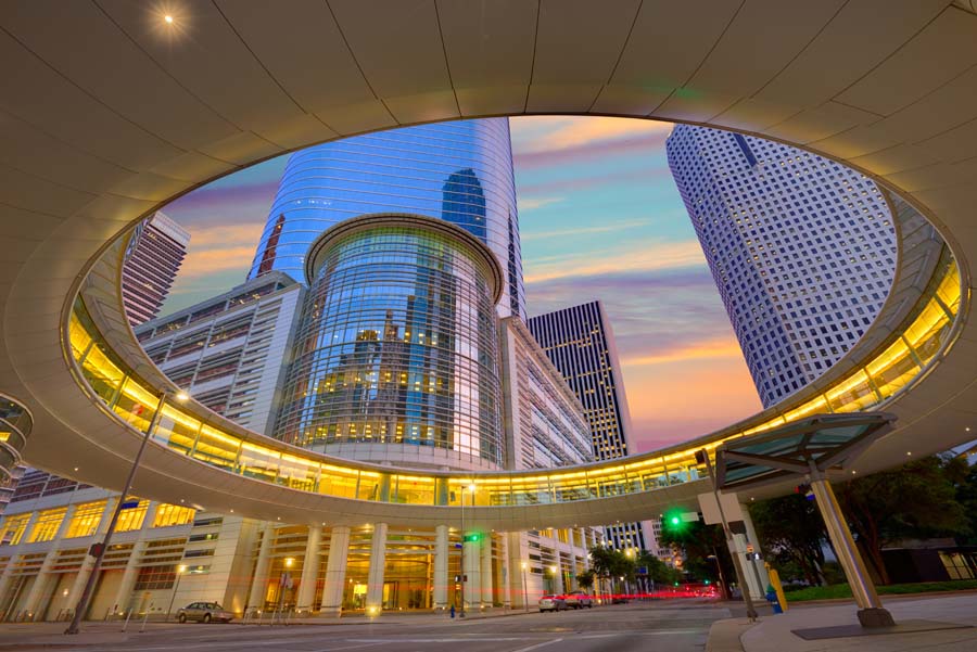 Downtown Houston skyscrapers viewed through a circular structure at dusk, highlighting modern architecture.